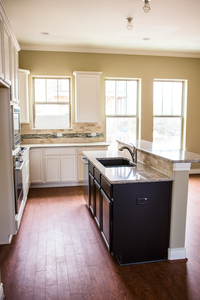 Mid-sized transitional l-shaped medium tone wood floor eat-in kitchen photo in Austin with an undermount sink, recessed-panel cabinets, white cabinets, granite countertops, beige backsplash, stone tile backsplash, stainless steel appliances and an island