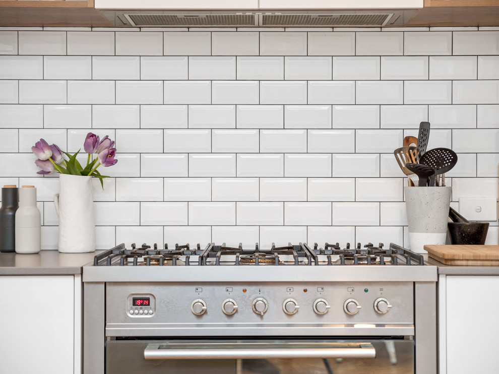 Exempel på ett litet modernt kök, med en enkel diskho, vita skåp, bänkskiva i koppar, vitt stänkskydd, stänkskydd i tunnelbanekakel, rostfria vitvaror, laminatgolv, en köksö och brunt golv