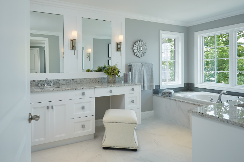 Design ideas for a mid-sized beach style master bathroom in Grand Rapids with recessed-panel cabinets, white cabinets, gray tile, glass tile, marble floors, engineered quartz benchtops, white floor, grey benchtops, a built-in vanity, a drop-in tub, grey walls and an undermount sink.