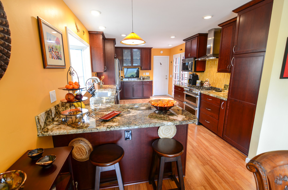 Large trendy galley medium tone wood floor eat-in kitchen photo in Tampa with a single-bowl sink, recessed-panel cabinets, red cabinets, granite countertops, yellow backsplash, glass tile backsplash and stainless steel appliances