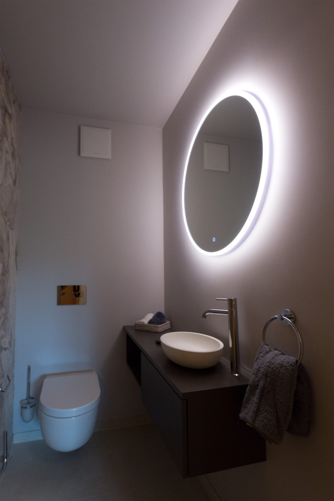 This is an example of a small contemporary bathroom in Berlin with flat-panel cabinets, grey cabinets, a wall-mount toilet, beige tile, grey walls, ceramic floors, a vessel sink, solid surface benchtops, beige floor, grey benchtops, a single vanity and a floating vanity.