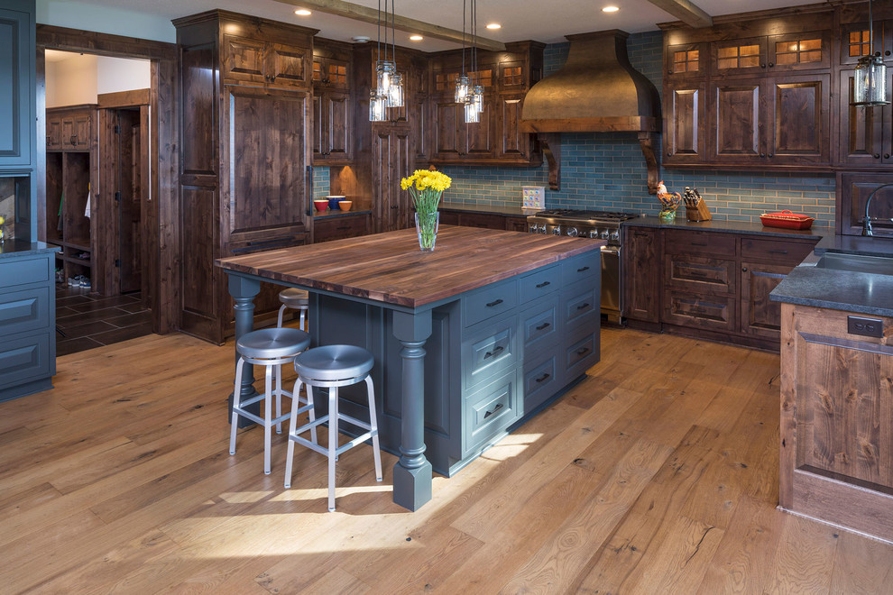 Photo of a country u-shaped kitchen in Minneapolis with raised-panel cabinets, medium wood cabinets, wood benchtops, blue splashback, subway tile splashback, panelled appliances, light hardwood floors, with island and brown floor.