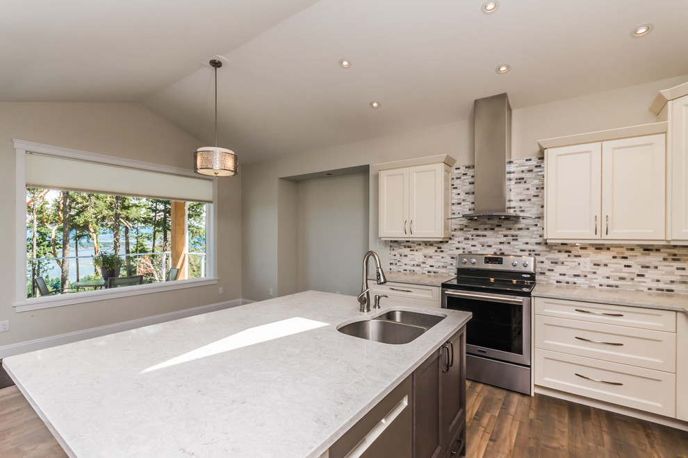 Photo of a mid-sized arts and crafts l-shaped eat-in kitchen in Vancouver with an undermount sink, shaker cabinets, white cabinets, quartzite benchtops, multi-coloured splashback, mosaic tile splashback, stainless steel appliances, laminate floors, with island, brown floor and white benchtop.