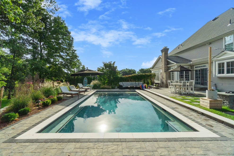 На фото: большой прямоугольный ландшафтный бассейн на заднем дворе в классическом стиле с покрытием из каменной брусчатки