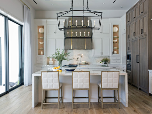 Modern kitchen with floor-to-ceiling pantry kitchen cabinets, integrated fridge panels, open display niches, marble backsplash, and a large island under a black lantern chandelier