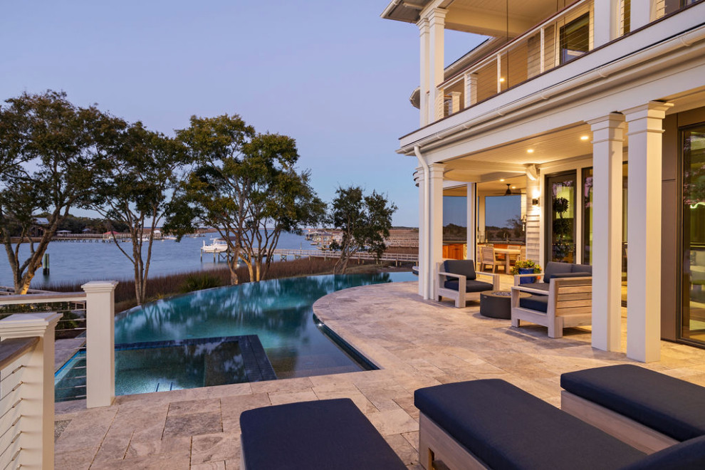Foto di un'ampia piscina a sfioro infinito stile marino personalizzata dietro casa con pavimentazioni in pietra naturale