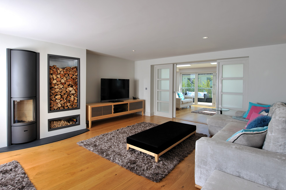 Foto de salón cerrado actual grande con paredes blancas, suelo de madera en tonos medios, estufa de leña, marco de chimenea de metal, televisor independiente y suelo marrón