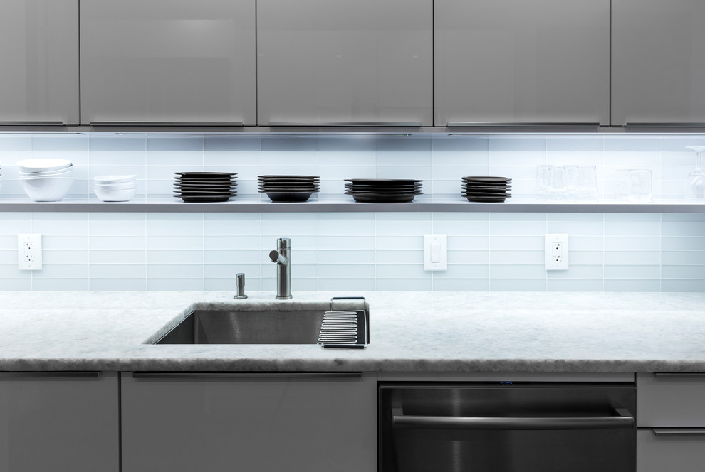 Photo of a small modern galley separate kitchen in New York with a drop-in sink, flat-panel cabinets, white cabinets, quartz benchtops, white splashback, glass tile splashback, stainless steel appliances, light hardwood floors and a peninsula.