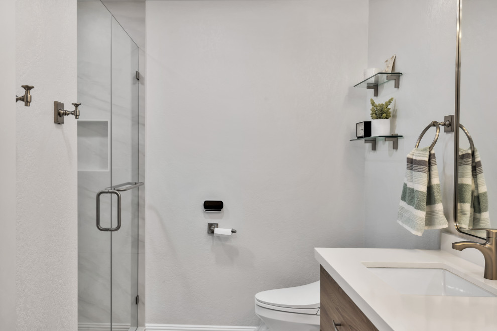 This is an example of a small midcentury 3/4 bathroom in San Diego with flat-panel cabinets, brown cabinets, an alcove shower, a two-piece toilet, gray tile, ceramic tile, grey walls, ceramic floors, an undermount sink, engineered quartz benchtops, grey floor, a hinged shower door, white benchtops, a double vanity, a floating vanity and brick walls.