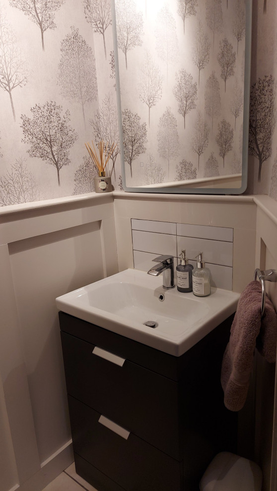 Inspiration for a small contemporary powder room in Dublin with flat-panel cabinets, black cabinets, a one-piece toilet, white tile, porcelain tile, multi-coloured walls, ceramic floors, an integrated sink, white floor, a freestanding vanity and wallpaper.