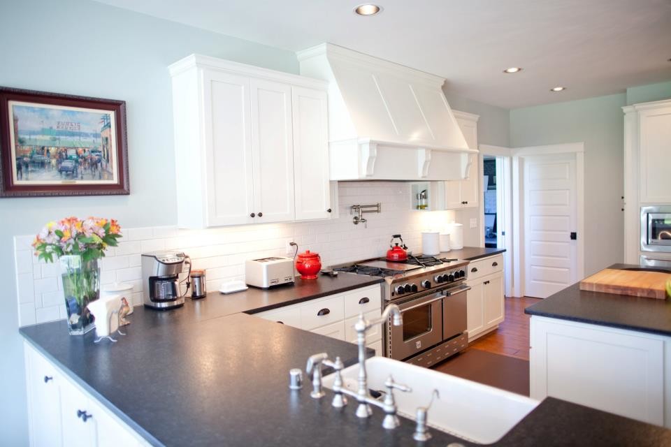 Example of a mid-sized transitional u-shaped light wood floor and brown floor eat-in kitchen design in Seattle with a farmhouse sink, recessed-panel cabinets, white cabinets, granite countertops, white backsplash, subway tile backsplash, stainless steel appliances and an island