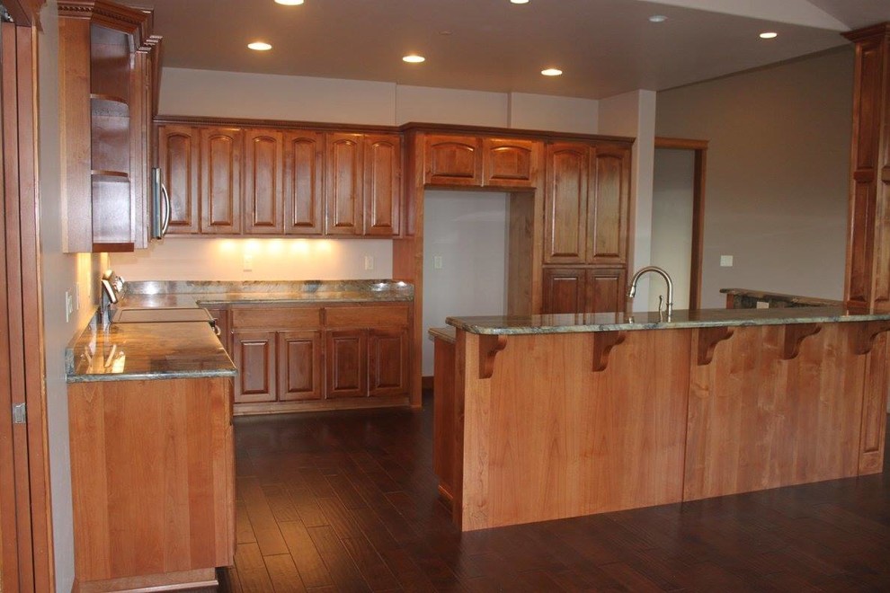 Large trendy l-shaped dark wood floor and brown floor kitchen photo with raised-panel cabinets, medium tone wood cabinets, granite countertops, stainless steel appliances and an island