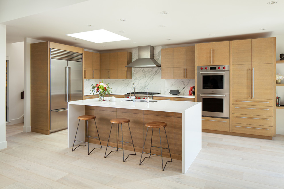 Photo of a large contemporary l-shaped open plan kitchen in San Francisco with an undermount sink, flat-panel cabinets, light wood cabinets, quartz benchtops, white splashback, marble splashback, stainless steel appliances, light hardwood floors, with island, white benchtop and beige floor.