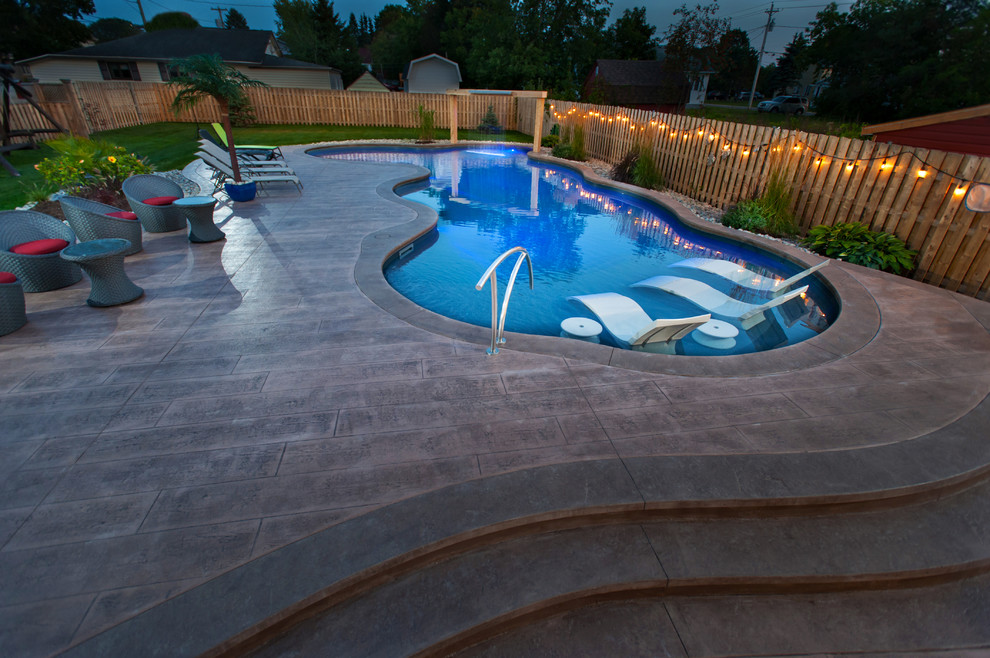 Design ideas for a large beach style side yard custom-shaped natural pool in Other with a pool house and stamped concrete.