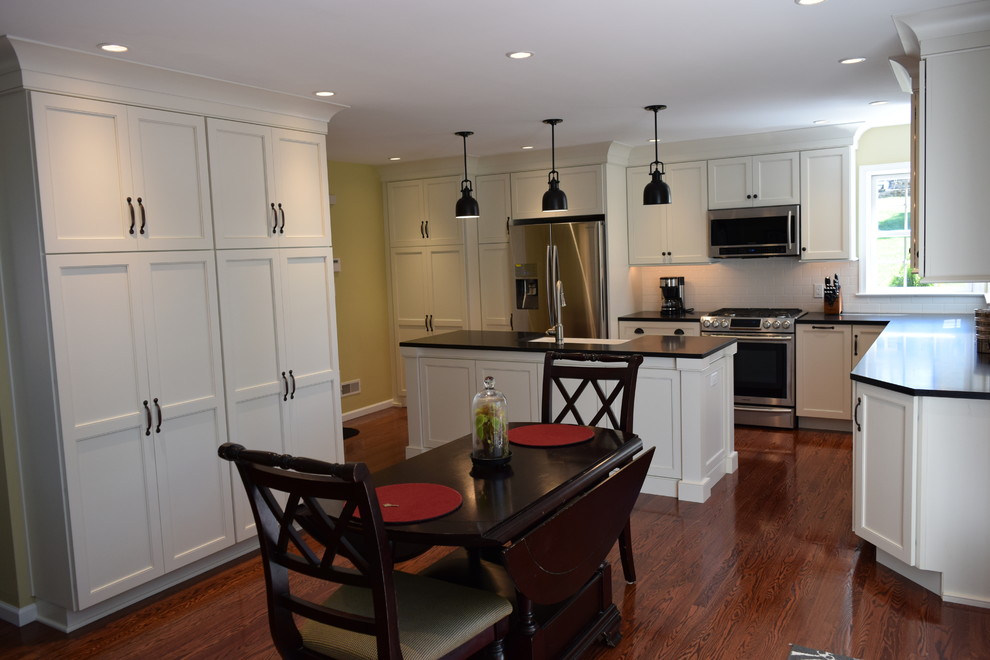 Example of a transitional medium tone wood floor kitchen design with an undermount sink, recessed-panel cabinets, white cabinets, quartz countertops, white backsplash, subway tile backsplash, stainless steel appliances and an island