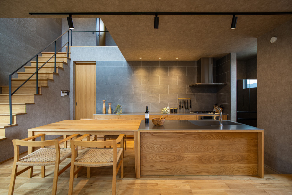 Imagen de cocina contemporánea abierta con fregadero integrado, armarios con paneles lisos, puertas de armario de madera clara, salpicadero verde, suelo de madera clara, una isla y encimeras grises