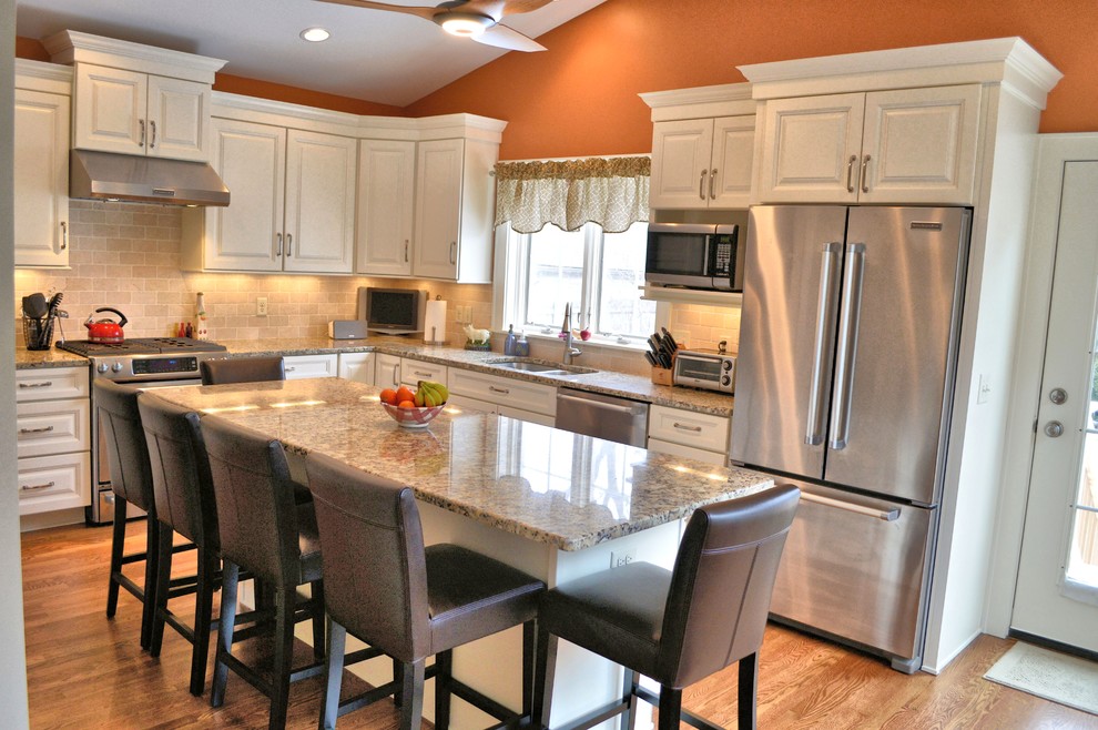Enclosed kitchen - large transitional l-shaped medium tone wood floor enclosed kitchen idea in Columbus with an undermount sink, raised-panel cabinets, white cabinets, granite countertops, beige backsplash, stone tile backsplash, stainless steel appliances and an island