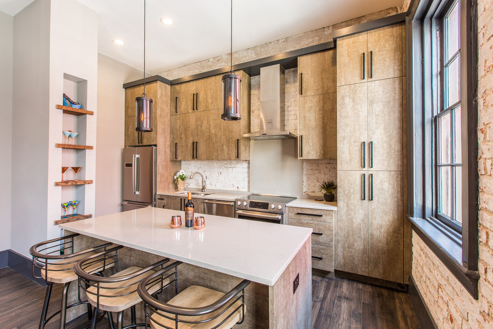 Photo of a contemporary single-wall kitchen in New Orleans with a drop-in sink, flat-panel cabinets, beige cabinets, white splashback, brick splashback, stainless steel appliances, dark hardwood floors, with island, brown floor and white benchtop.