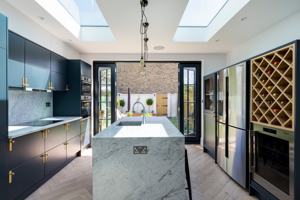 This is an example of a mid-sized contemporary galley separate kitchen in London with flat-panel cabinets, blue cabinets, marble benchtops, white splashback, marble splashback, stainless steel appliances, light hardwood floors, an undermount sink, with island and beige floor.