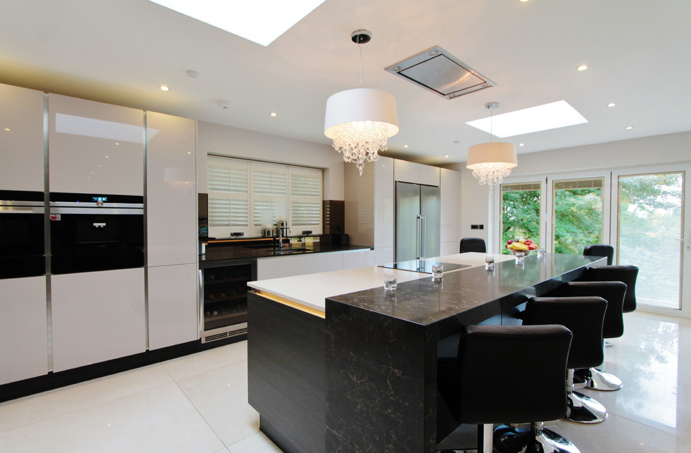 Photo of a large contemporary single-wall open plan kitchen in London with an undermount sink, flat-panel cabinets, white cabinets, quartzite benchtops, black appliances, porcelain floors, with island, white floor and white benchtop.