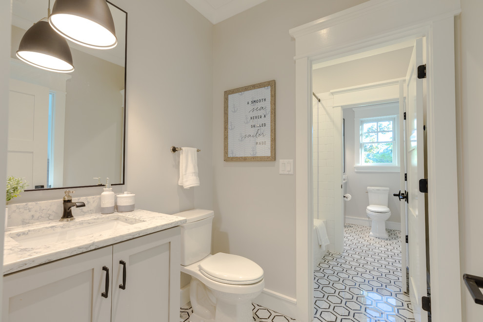 Photo of a mid-sized beach style kids bathroom in Other with recessed-panel cabinets, an alcove tub, an alcove shower, a two-piece toilet, white tile, marble, grey walls, marble floors, an undermount sink, engineered quartz benchtops, multi-coloured floor, a sliding shower screen, white benchtops and white cabinets.
