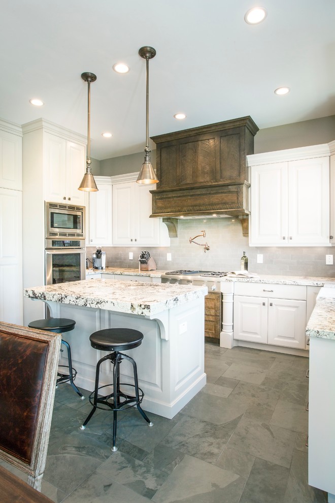 Inspiration for a mid-sized country u-shaped eat-in kitchen in Salt Lake City with a farmhouse sink, raised-panel cabinets, white cabinets, granite benchtops, grey splashback, subway tile splashback, stainless steel appliances, slate floors, with island, grey floor and multi-coloured benchtop.