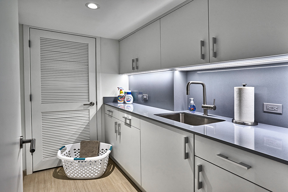 Design ideas for a large modern galley utility room in Chicago with a single-bowl sink, flat-panel cabinets, white cabinets, quartz benchtops, white walls, porcelain floors, a stacked washer and dryer, beige floor and grey benchtop.