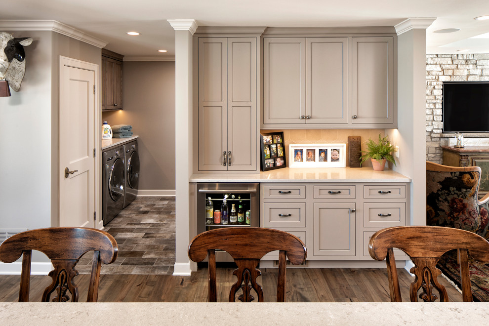 Inspiration for a small country single-wall home bar in Minneapolis with no sink, recessed-panel cabinets, beige cabinets, beige splashback, ceramic splashback, medium hardwood floors, brown floor, white benchtop and granite benchtops.