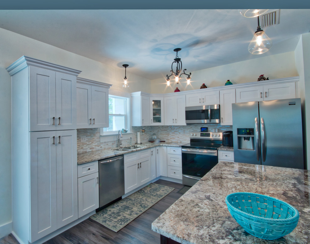 Example of a mid-sized l-shaped eat-in kitchen design with an undermount sink, shaker cabinets, yellow cabinets, granite countertops, glass tile backsplash, stainless steel appliances, an island and white countertops