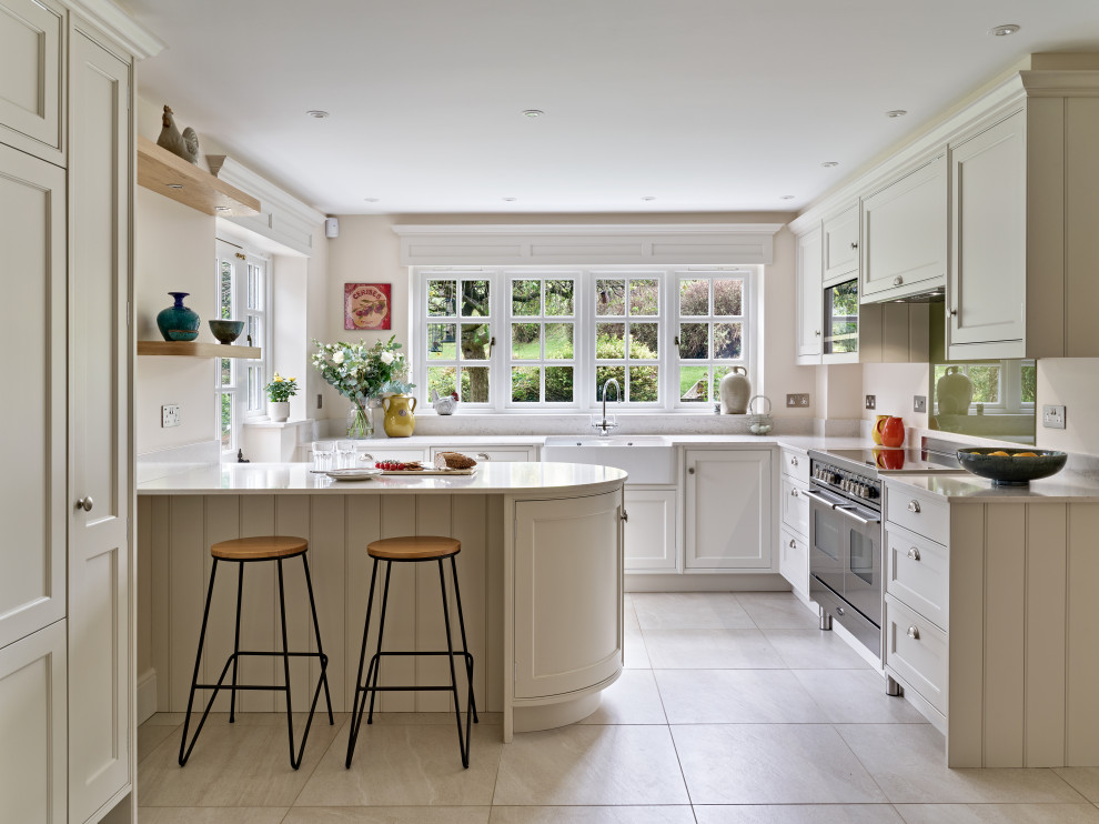 Inspiration for a mid-sized traditional u-shaped separate kitchen in Buckinghamshire with shaker cabinets, beige cabinets, quartz benchtops, beige splashback, glass sheet splashback, stainless steel appliances, porcelain floors, a peninsula, beige floor, beige benchtop and a farmhouse sink.