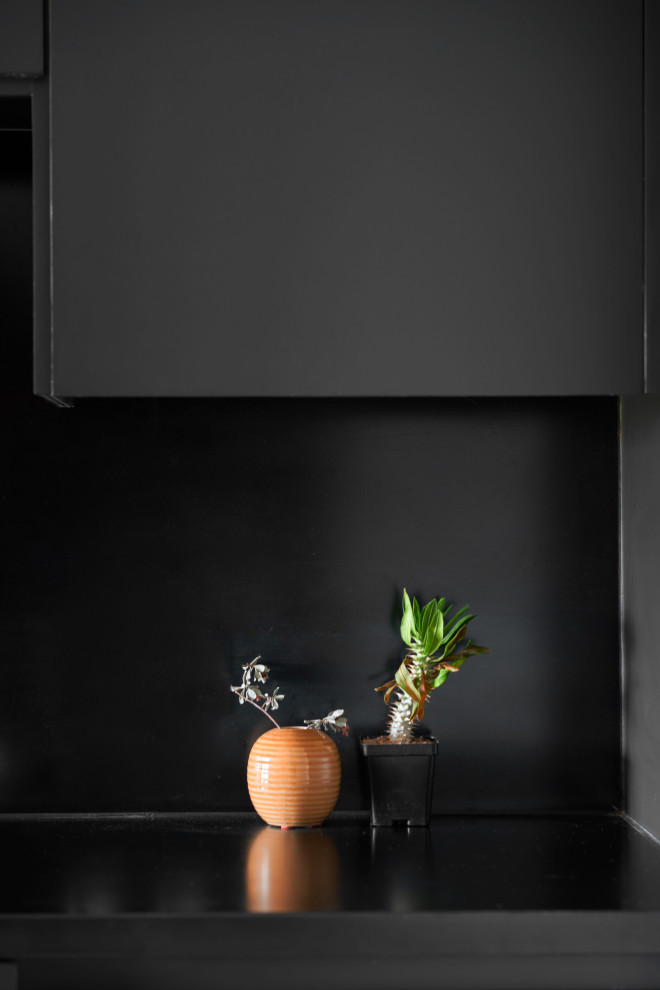 Modern inredning av ett litet svart linjärt svart kök och matrum, med en undermonterad diskho, släta luckor, svarta skåp, bänkskiva i akrylsten, svart stänkskydd, svarta vitvaror, klinkergolv i keramik och svart golv