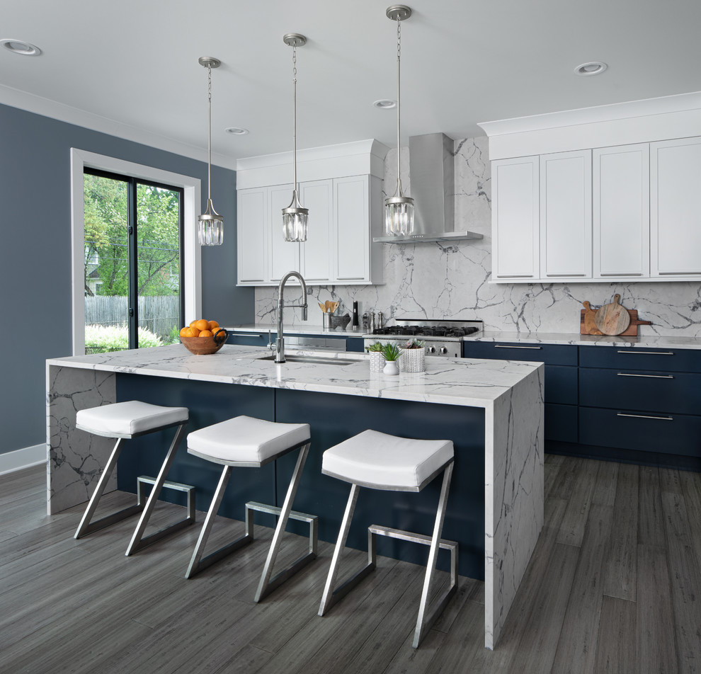This is an example of a transitional u-shaped kitchen in Other with an undermount sink, shaker cabinets, blue cabinets, quartz benchtops, grey splashback, stainless steel appliances, light hardwood floors, with island, grey benchtop and grey floor.