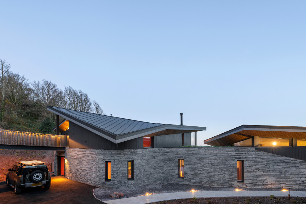 This is an example of a large contemporary house exterior in Devon with stone veneer, a butterfly roof, a metal roof and a black roof.
