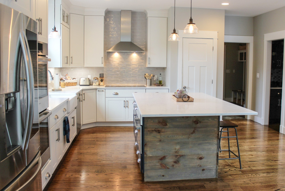 Transitional l-shaped medium tone wood floor and brown floor kitchen pantry photo with a farmhouse sink, recessed-panel cabinets, white cabinets, quartz countertops, gray backsplash, porcelain backsplash, stainless steel appliances, an island and white countertops