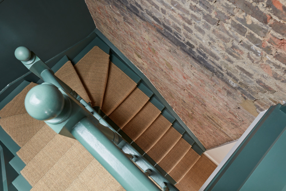 Cette image montre un escalier bohème en U avec des marches en moquette, des contremarches en moquette, un garde-corps en bois et un mur en parement de brique.