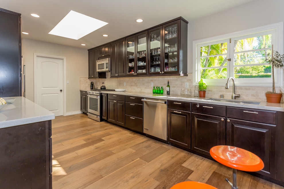 Inspiration for a large transitional galley eat-in kitchen in Los Angeles with raised-panel cabinets, dark wood cabinets, quartzite benchtops, beige splashback, stone tile splashback, no island, an undermount sink, stainless steel appliances, medium hardwood floors and brown floor.