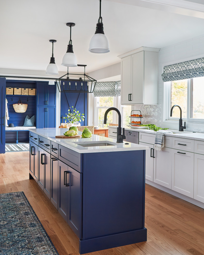Inredning av ett klassiskt stort vit vitt kök, med en undermonterad diskho, skåp i shakerstil, blå skåp, bänkskiva i kvartsit, vitt stänkskydd, stänkskydd i porslinskakel, rostfria vitvaror, mellanmörkt trägolv, en köksö och brunt golv