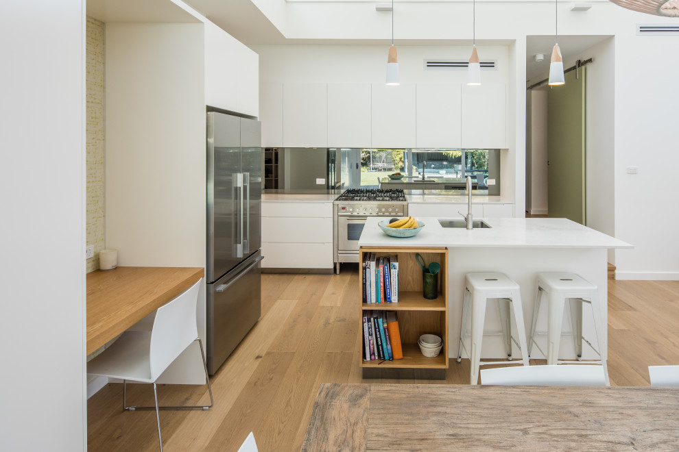 Inspiration for a contemporary l-shaped eat-in kitchen in Sydney with an undermount sink, flat-panel cabinets, white cabinets, stainless steel appliances, with island, brown floor, white benchtop, quartz benchtops, grey splashback, glass sheet splashback and light hardwood floors.