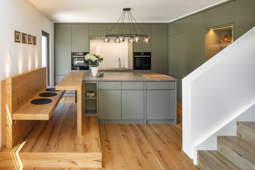 This is an example of a large contemporary open plan kitchen in Munich with light hardwood floors and with island.