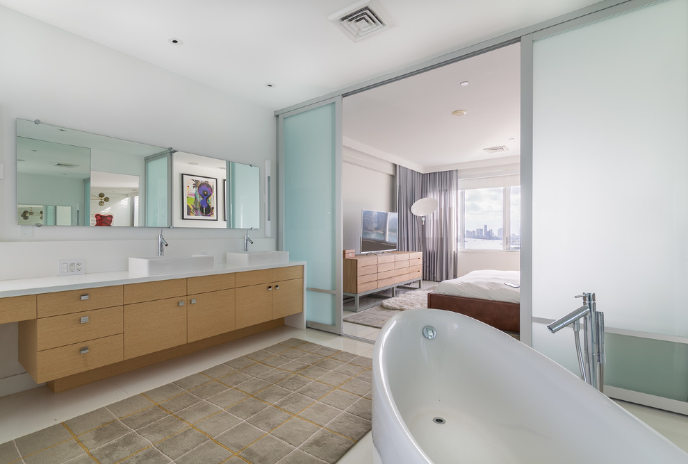 This is an example of a large contemporary master bathroom in Miami with an integrated sink, flat-panel cabinets, light wood cabinets, a freestanding tub, a corner shower, a one-piece toilet, white tile and white walls.
