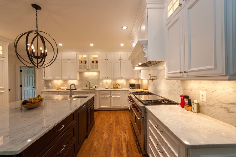 This is an example of a large transitional l-shaped open plan kitchen in DC Metro with an undermount sink, recessed-panel cabinets, white cabinets, marble benchtops, grey splashback, stone slab splashback, stainless steel appliances, dark hardwood floors, with island and brown floor.