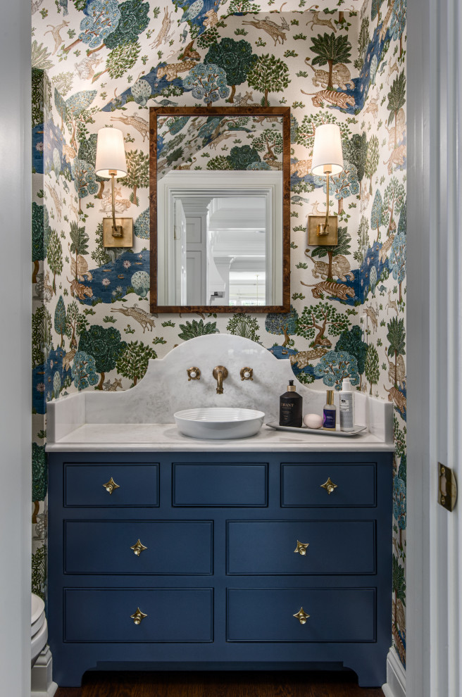 Small transitional powder room in Nashville with beaded inset cabinets, blue cabinets, medium hardwood floors, a vessel sink, a built-in vanity, wallpaper, wallpaper, multi-coloured walls, brown floor and white benchtops.