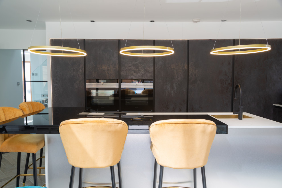 This is an example of a mid-sized contemporary l-shaped eat-in kitchen in Essex with a single-bowl sink, glass benchtops and black benchtop.