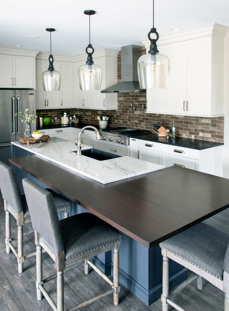 L-shaped gray floor kitchen photo with a farmhouse sink, white cabinets, quartz countertops, beige backsplash, ceramic backsplash, stainless steel appliances and an island