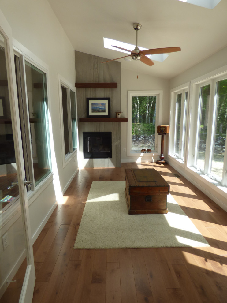 Photo of a contemporary sunroom in Other with medium hardwood floors, a standard fireplace, a tile fireplace surround, a skylight and brown floor.