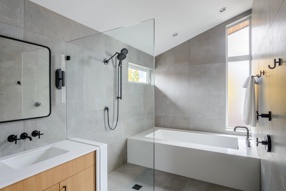 This is an example of a mid-sized contemporary master bathroom in Seattle with flat-panel cabinets, light wood cabinets, an alcove tub, a curbless shower, a two-piece toilet, gray tile, porcelain tile, grey walls, porcelain floors, an undermount sink, engineered quartz benchtops, grey floor, an open shower, white benchtops, an enclosed toilet, a double vanity, a floating vanity and vaulted.