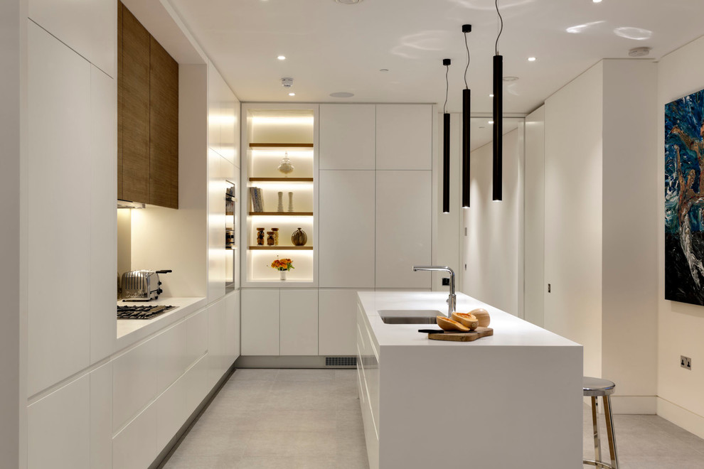 This is an example of a large contemporary l-shaped open plan kitchen in London with a double-bowl sink, flat-panel cabinets, white cabinets, solid surface benchtops, beige splashback, glass sheet splashback, stainless steel appliances, ceramic floors, with island, grey floor and white benchtop.