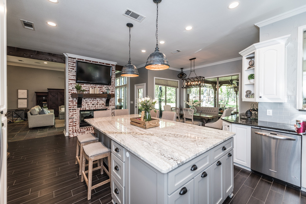 This is an example of a large country u-shaped eat-in kitchen in Dallas with an undermount sink, raised-panel cabinets, white cabinets, granite benchtops, blue splashback, ceramic splashback, stainless steel appliances, porcelain floors, with island and brown floor.