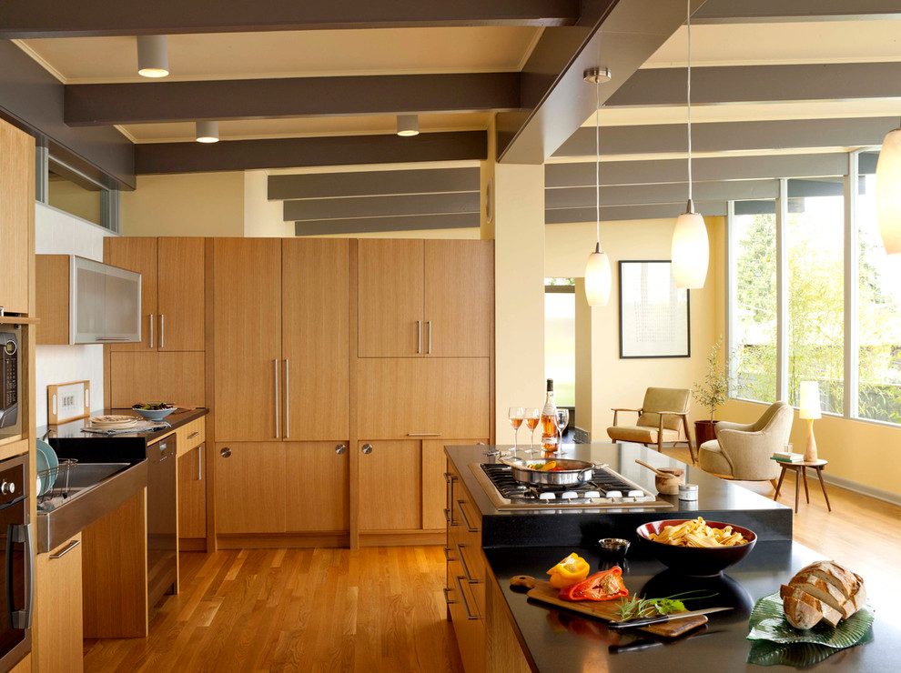 Photo of a large midcentury l-shaped kitchen in Seattle with flat-panel cabinets, medium wood cabinets, a farmhouse sink, soapstone benchtops, stainless steel appliances, medium hardwood floors, with island and black benchtop.