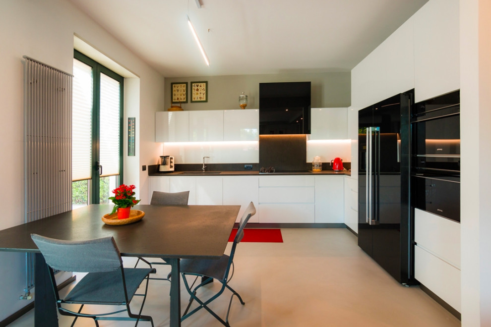 This is an example of a contemporary l-shaped open plan kitchen in Milan with an undermount sink, flat-panel cabinets, white cabinets, black splashback, black appliances, no island, white floor and black benchtop.
